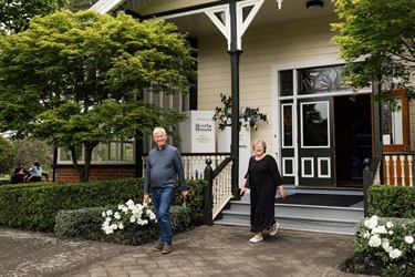 image shows two happy old people stepping out of a historical homestead